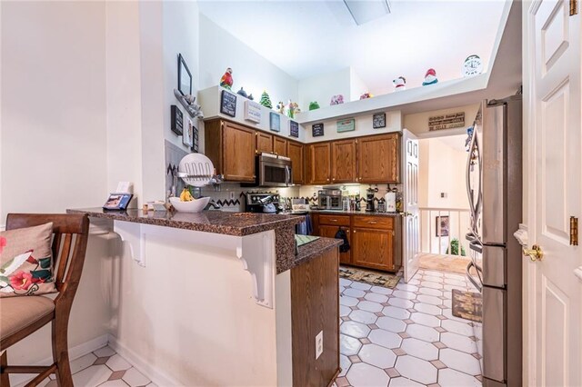 kitchen featuring stainless steel appliances, kitchen peninsula, dark stone counters, and a breakfast bar