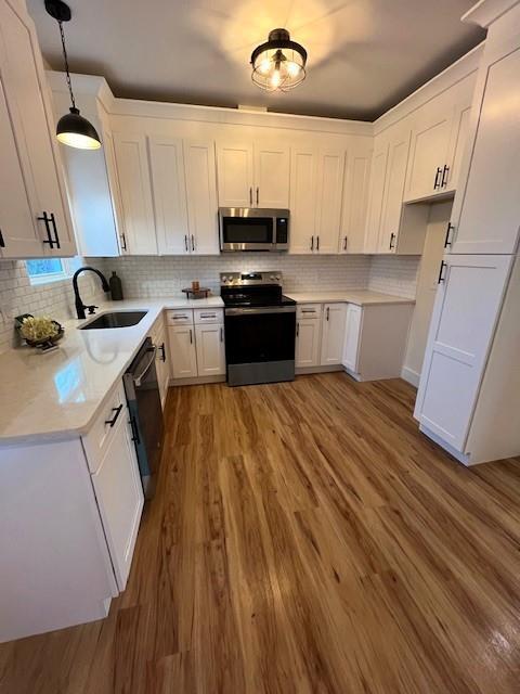 kitchen featuring sink, white cabinetry, decorative light fixtures, light wood-type flooring, and appliances with stainless steel finishes