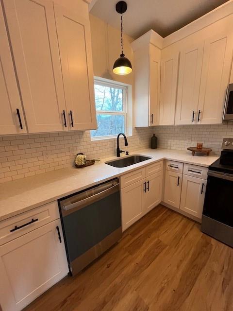 kitchen with appliances with stainless steel finishes, sink, pendant lighting, and white cabinets