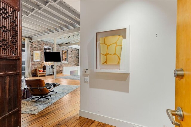 hallway featuring brick wall, beamed ceiling, wood finished floors, and baseboards