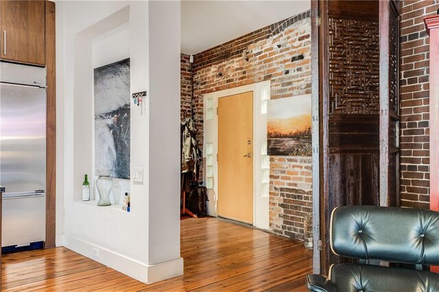 corridor with baseboards, brick wall, and wood finished floors