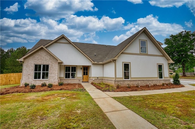 view of front facade featuring a shingled roof, brick siding, fence, and a front lawn