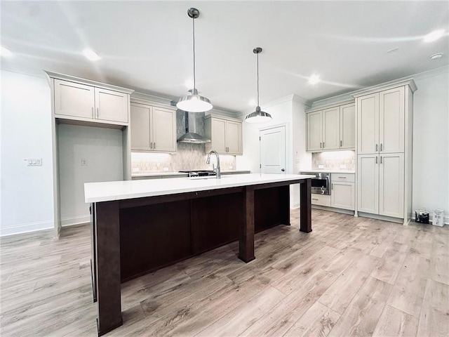 kitchen featuring a kitchen island with sink, pendant lighting, wall chimney range hood, and light wood-type flooring