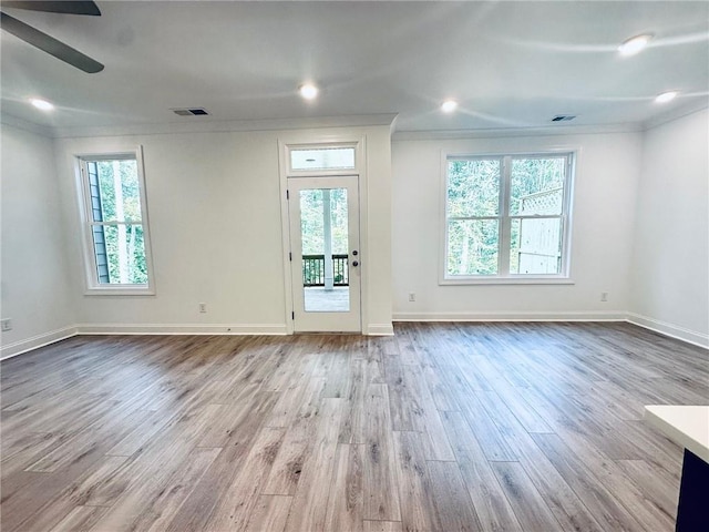 empty room featuring ceiling fan, plenty of natural light, ornamental molding, and light wood-type flooring