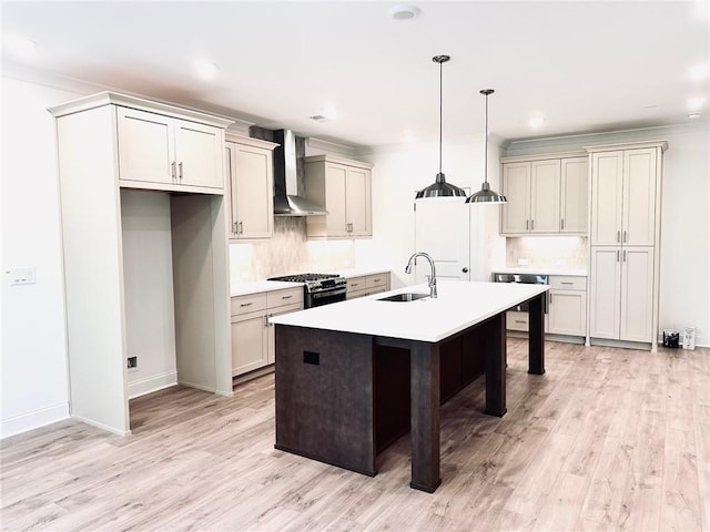 kitchen featuring stainless steel range with gas cooktop, sink, wall chimney exhaust hood, light wood-type flooring, and an island with sink