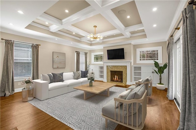 living room featuring wood finished floors, coffered ceiling, a warm lit fireplace, ornamental molding, and a notable chandelier