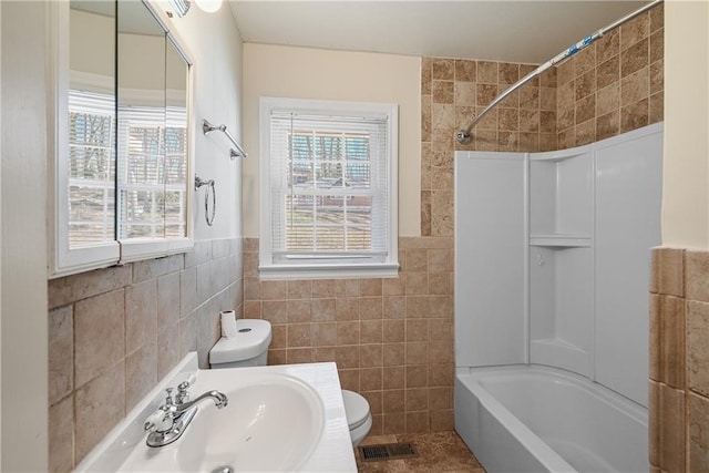 bathroom featuring toilet, a sink, visible vents, tile walls, and tub / shower combination