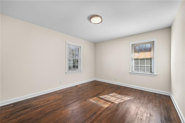 spare room with baseboards, dark wood-type flooring, and a healthy amount of sunlight