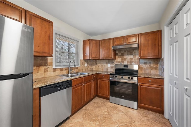 kitchen featuring brown cabinets, appliances with stainless steel finishes, a sink, light stone countertops, and under cabinet range hood