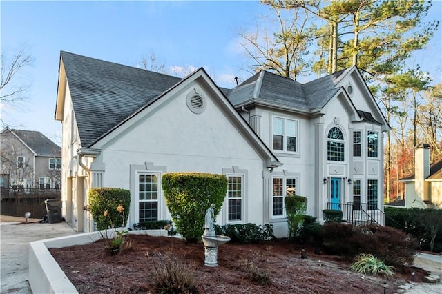 view of front of home with fence, roof with shingles, and stucco siding