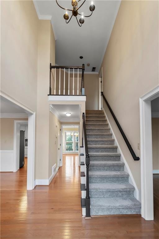 staircase featuring baseboards, crown molding, a towering ceiling, and wood finished floors