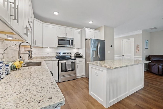 kitchen with a center island, appliances with stainless steel finishes, white cabinets, a sink, and wood finished floors