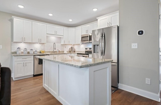 kitchen with appliances with stainless steel finishes, white cabinetry, a sink, and wood finished floors