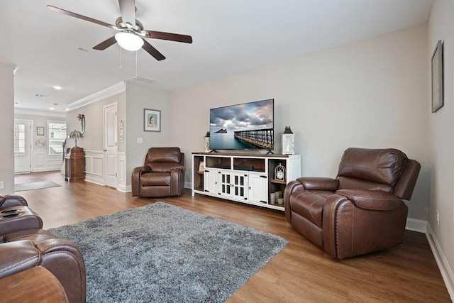 living room featuring ceiling fan, baseboards, wood finished floors, and crown molding