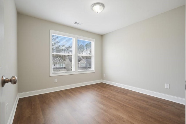 spare room featuring dark wood-style flooring, visible vents, and baseboards