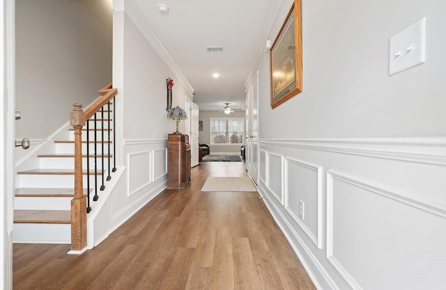 hallway with crown molding, visible vents, a decorative wall, stairway, and wood finished floors