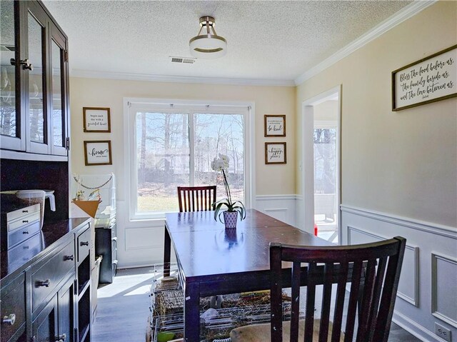 dining area featuring visible vents, wainscoting, a textured ceiling, and crown molding