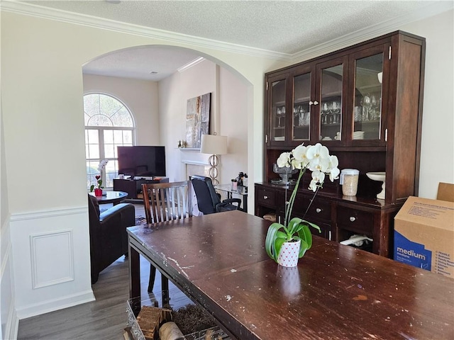 dining space with dark wood finished floors, arched walkways, a wainscoted wall, a textured ceiling, and crown molding
