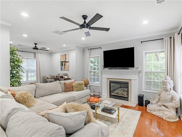 living room with ceiling fan, a high end fireplace, ornamental molding, and light hardwood / wood-style floors