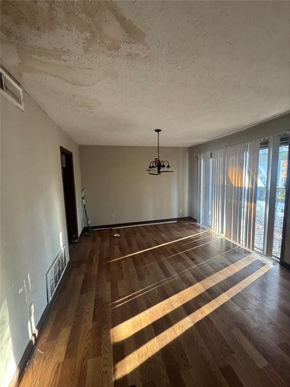 unfurnished dining area with a notable chandelier, a textured ceiling, and dark hardwood / wood-style flooring