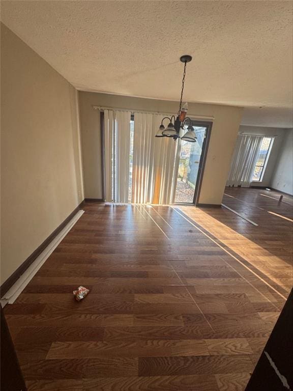 unfurnished dining area with dark hardwood / wood-style flooring, a notable chandelier, and a textured ceiling