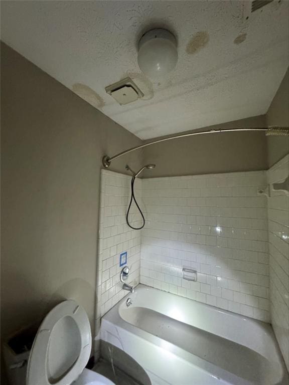 bathroom featuring a textured ceiling, tiled shower / bath combo, and toilet