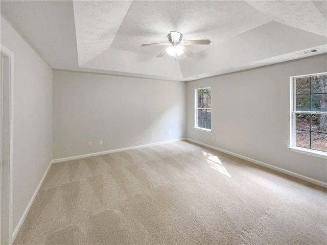 empty room with a raised ceiling, light colored carpet, ceiling fan, and a textured ceiling