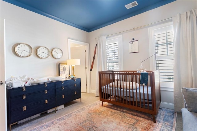 bedroom with baseboards, visible vents, a crib, and light carpet