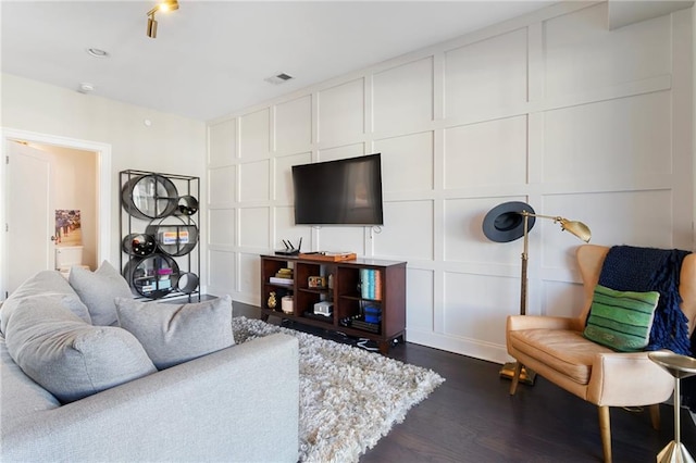 living area featuring visible vents, dark wood-style flooring, and a decorative wall