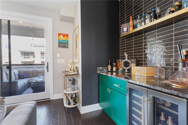 bar featuring beverage cooler, a bar, baseboards, dark wood finished floors, and backsplash