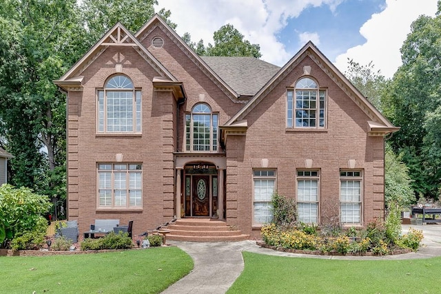 view of front of property with brick siding, a front lawn, and a shingled roof