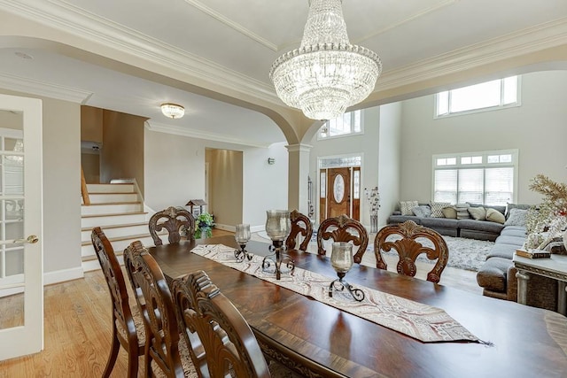 dining room featuring arched walkways, crown molding, light wood-style floors, ornate columns, and stairs