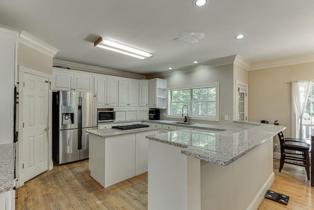 kitchen featuring light wood finished floors, ornamental molding, a peninsula, stainless steel appliances, and a sink