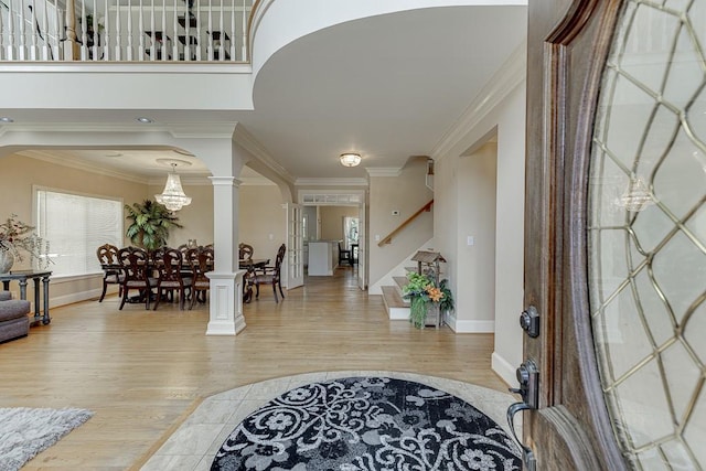 entryway featuring arched walkways, ornamental molding, stairway, light wood finished floors, and ornate columns