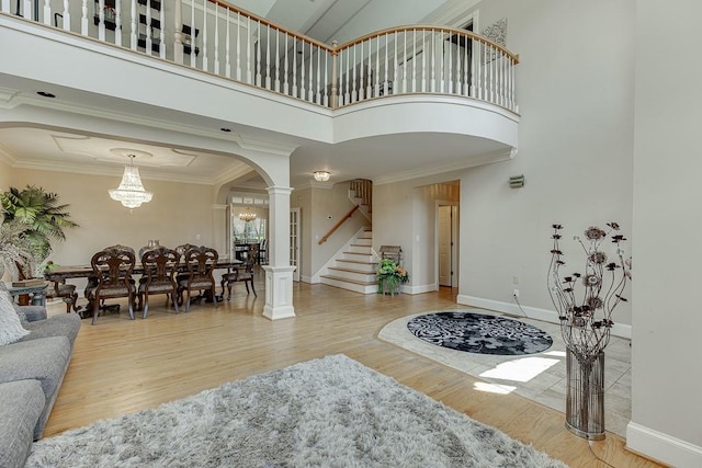 entrance foyer featuring arched walkways, crown molding, stairway, light wood-style flooring, and ornate columns