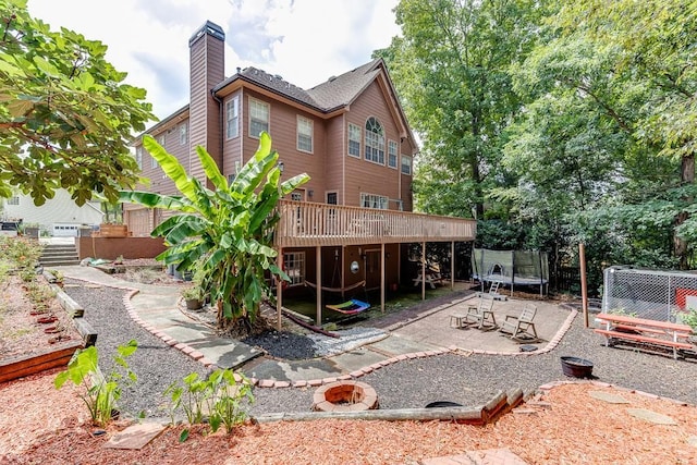 back of house with an outdoor fire pit, a chimney, a trampoline, a deck, and a patio area