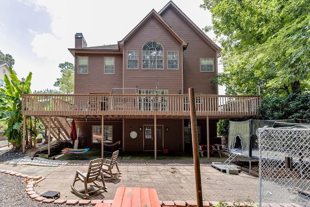 back of house featuring a trampoline, a chimney, a deck, and a patio