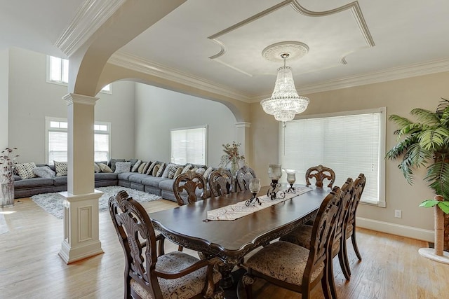 dining room with light wood-type flooring, ornate columns, arched walkways, and crown molding