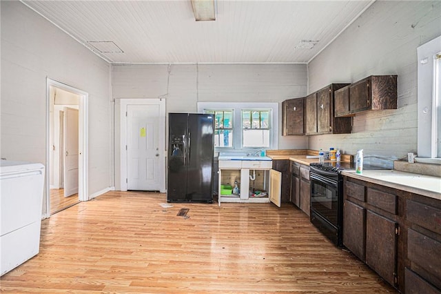 kitchen featuring black appliances, washer / dryer, dark brown cabinets, and light hardwood / wood-style floors