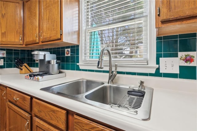 kitchen with brown cabinetry, light countertops, a sink, and decorative backsplash