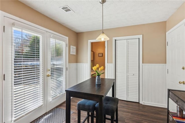 dining space featuring french doors, a wainscoted wall, visible vents, dark wood-type flooring, and a textured ceiling