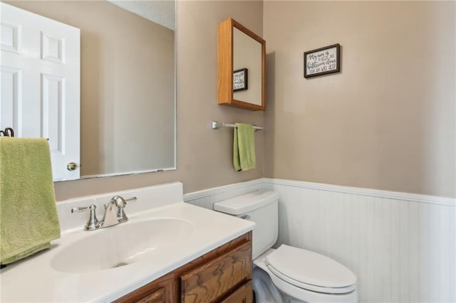 half bath featuring toilet, vanity, and wainscoting