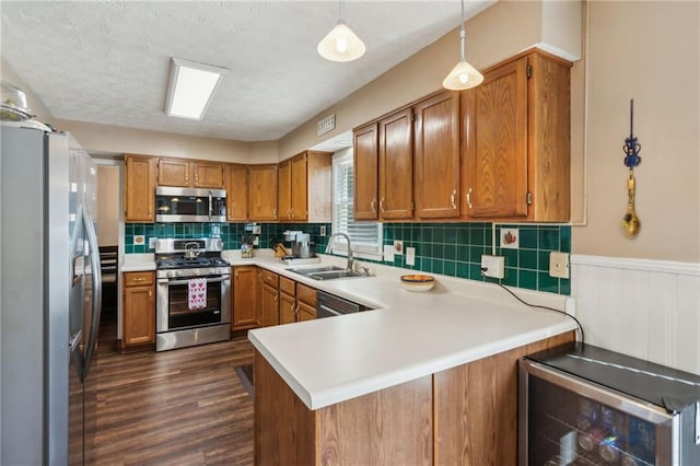 kitchen with wine cooler, a peninsula, a sink, appliances with stainless steel finishes, and brown cabinets