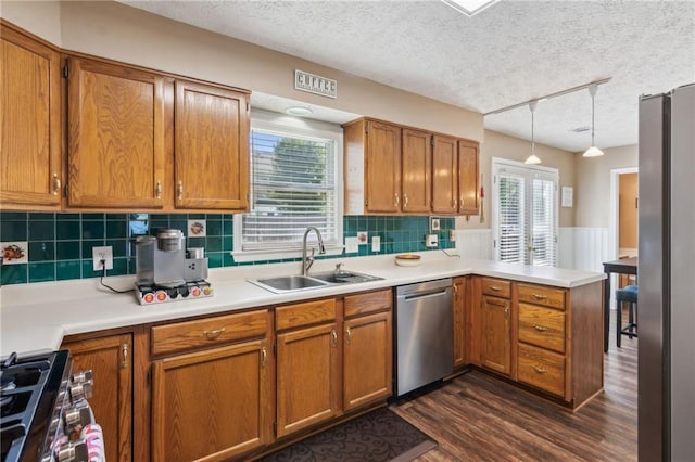 kitchen featuring appliances with stainless steel finishes, brown cabinetry, a sink, and a peninsula