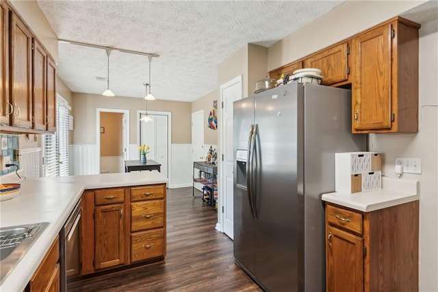 kitchen with dark wood-style floors, a wainscoted wall, stainless steel appliances, brown cabinetry, and a peninsula