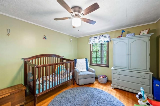 bedroom featuring hardwood / wood-style flooring, ceiling fan, a nursery area, ornamental molding, and a textured ceiling