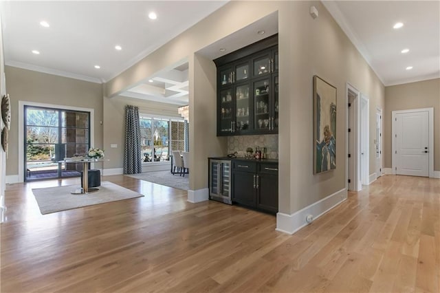 bar with light wood-style floors, ornamental molding, a dry bar, and baseboards