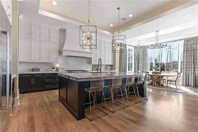 kitchen featuring light wood-style floors, a raised ceiling, premium range hood, and a sink