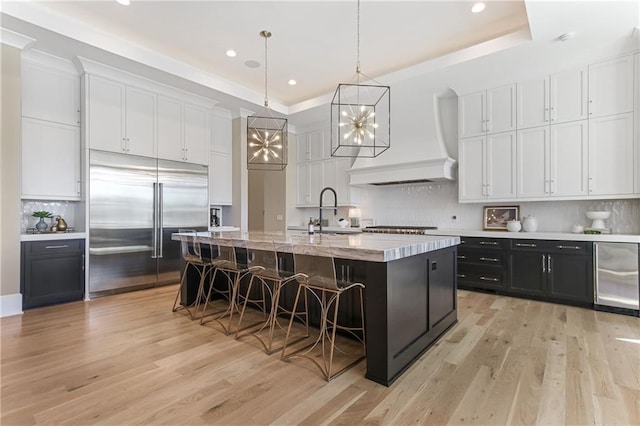 kitchen featuring white cabinetry, dark cabinetry, a large island, stainless steel built in fridge, and custom range hood