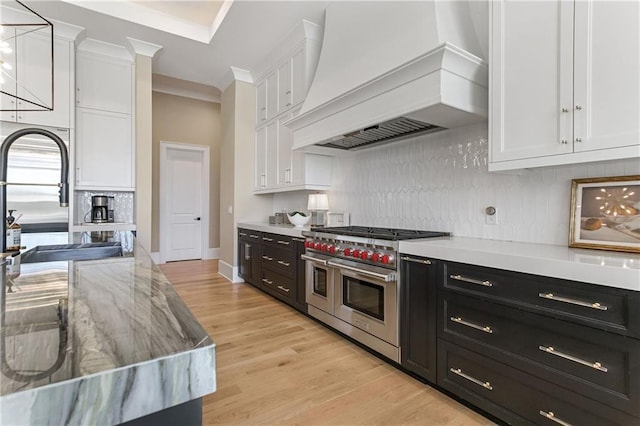 kitchen with dark cabinetry, range with two ovens, white cabinets, and custom range hood